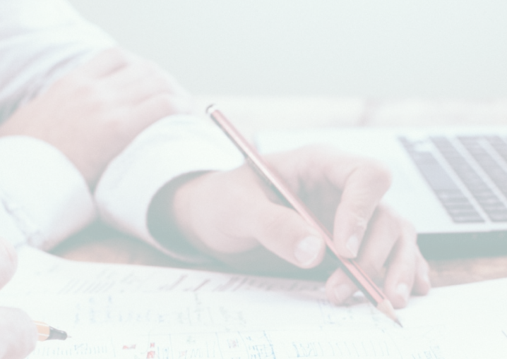 person writing with pencil in front of laptop